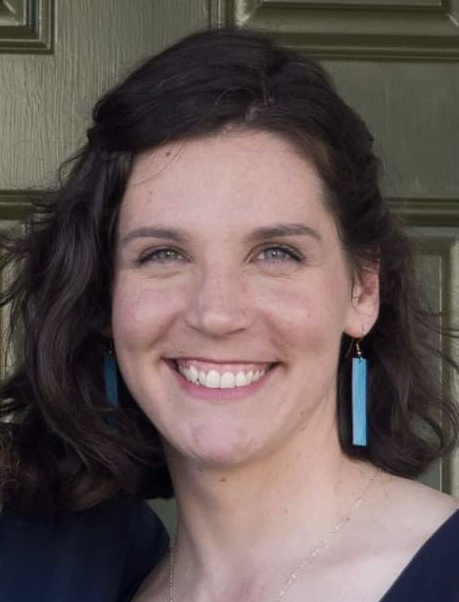 A photo of Cat Dayger, who has brown hair, light blue eyes, and is wearing blue rectangular earrings. 