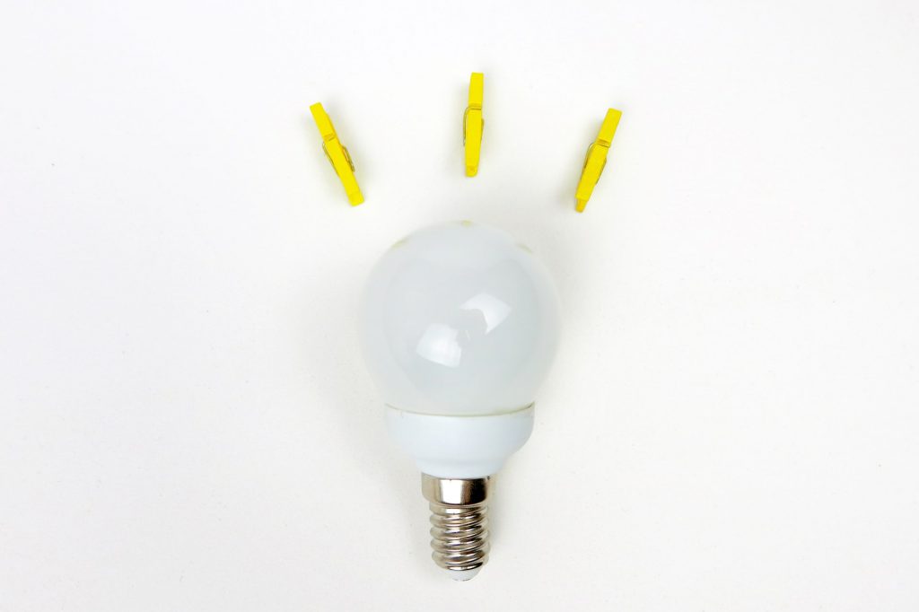 A lightbulb on a white background. Three yellow clothes-pegs are arranged around the top to convey the idea that the lightbulb is "on," even though it isn't. 