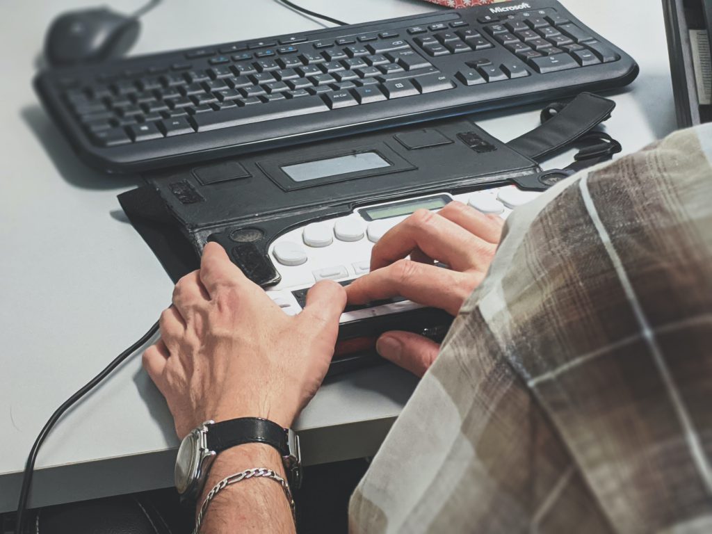 A view from behind of a person using a braille writer to interact with their computer. 