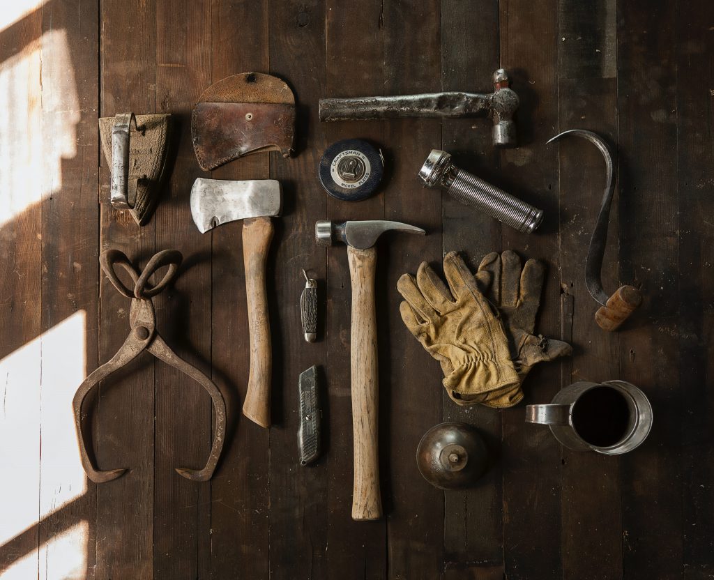 A table with various tools laid out, including a hammer, and axe, and some work gloves.